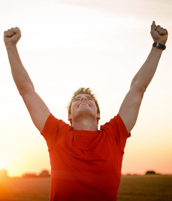 A man with arms in the air celebrates in the glow of sunset