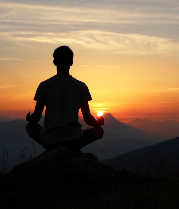 Seated man meditating on mountain at sunrise or sunset